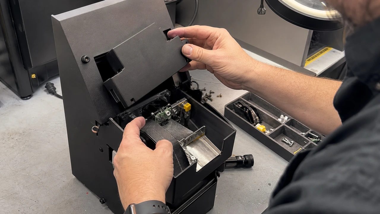 Technician calibrating infrared optical coin counting sensors, anti-reverse payout baffles, and hopper security shields