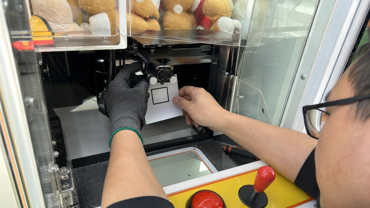 Technician calibrating infrared beam curtain sensors at claw machine prize drop chute to ensure accurate payout confirmation